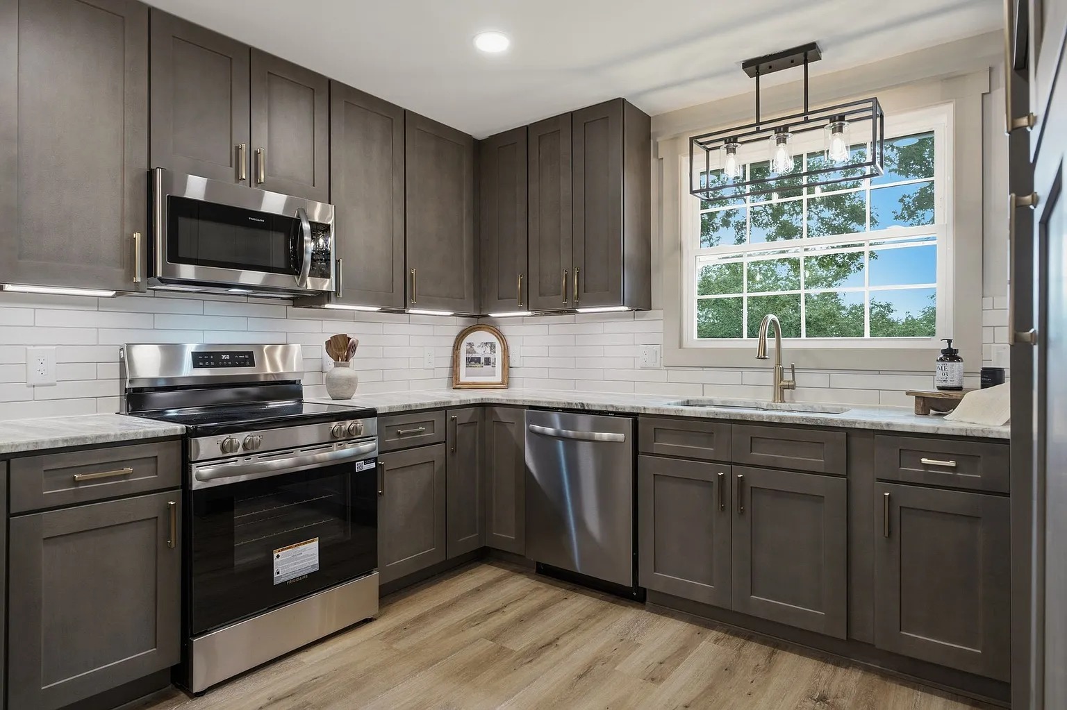 Custom grey-brown shaker kitchen with stainless appliances and a bright window by Ranger Renovations